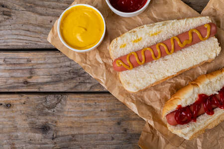 Overhead view of hot dogs with tomato and mustered sauces on paper bags at table. unaltered, unhealthy food, meat, bread, sausage, dipping sauce and fast food.の写真素材
