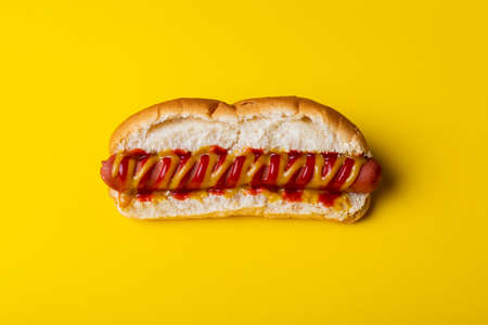 Close-up of hot dog on yellow background. unaltered, unhealthy food, meat, bread, sausage, sauce and fast food.の写真素材