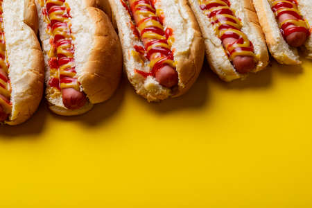 High angle view of sauces on hot dogs arranged side by side on yellow background. unaltered, unhealthy food, copy space, meat, bread, arrangement, sausage, sauce and fast food.の写真素材