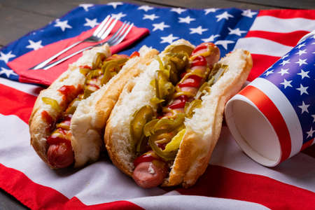Close-up of hot dogs with jalapeno served on american flag with fork and disposable cups. unaltered, unhealthy food, meat, bread, sausage and fast food.の写真素材