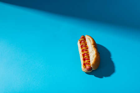 Close-up of hot dog with mustered and tomato sauce against blue background with copy space. unaltered, unhealthy food, meat, bread, shadow, sausage and fast food.の写真素材