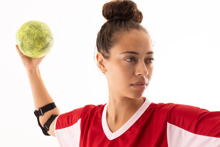 Close-up of biracial young female handball player throwing ball against white background. unaltered,...