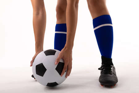 Low section of biracial female player holding soccer ball while standing against white background. white background, unaltered, sport, soccer shoe, sock, athlete and women's soccer.の写真素材