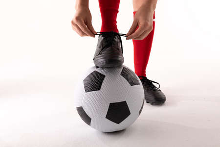Close-up of caucasian young female player tying soccer shoe lace while standing with foot on ball. white background, unaltered, sport, soccer shoe, sock, athlete and women's soccer.の写真素材