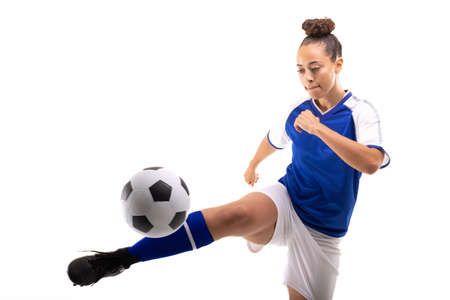 Biracial young female player kicking soccer ball while playing soccer against white background. unaltered, sport, copy space, sports uniform, athlete and women&#39;s soccer.の写真素材