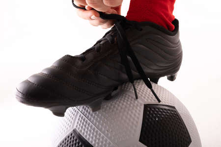 Extreme close-up of caucasian young female player tying shoe lace with foot on soccer ball. white...