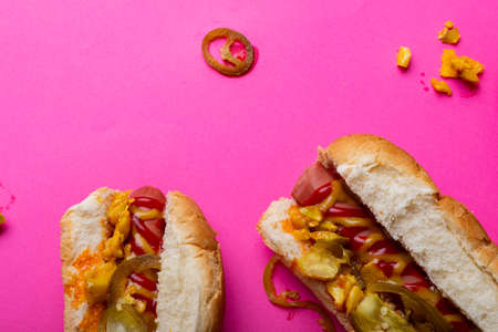 Overhead close-up of hot dogs on pink background. unaltered, unhealthy food, meat, bread, sausage, sauce, jalapeno and fast food.の写真素材