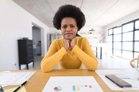 Portrait of serious african american mid adult female freelancer with chart sitting at home office. unaltered, working at home, freelance work, home office and business concept.の写真素材