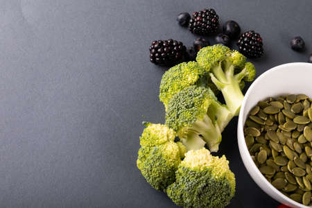 High angle close-up of broccolis by pumpkin seeds in bowl with blueberries and blackberries on...
