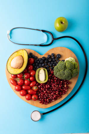 Directly above view of healthy food on heart shaped cutting board by stethoscope on blue background. unaltered, healthy eating, food, organic, healthcare, copy space.の写真素材
