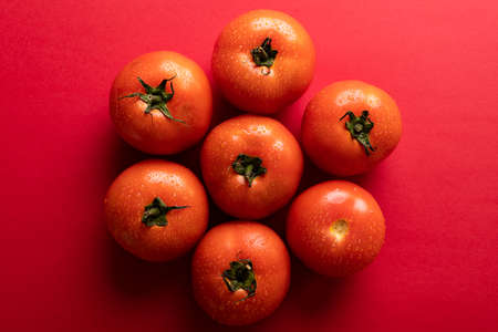 Overhead view of fresh red tomatoes with water drops arranged on colored background. unaltered,...