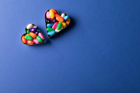 Directly above view of heart shape containers with colorful candies by copy space on blue...