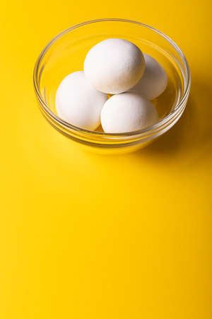 High angle view of fresh white eggs in glass bowl over yellow background with copy space. unaltered,...