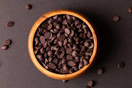 Directly above view of fresh chocolate chips in wooden bowl over colored background. unaltered,...