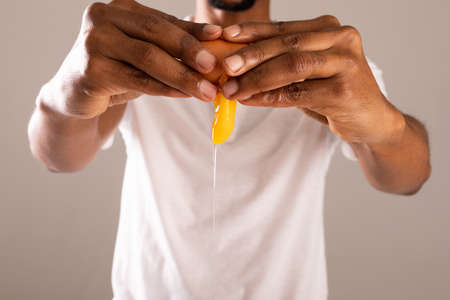 Midsection of man breaking egg shell against gray background. unaltered, food, healthy eating and organic concept.の写真素材