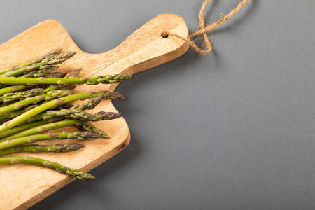 High angle view of fresh asparagus on wooden cutting board by copy space against gray background. unaltered, food, healthy eating and organic concept.の写真素材