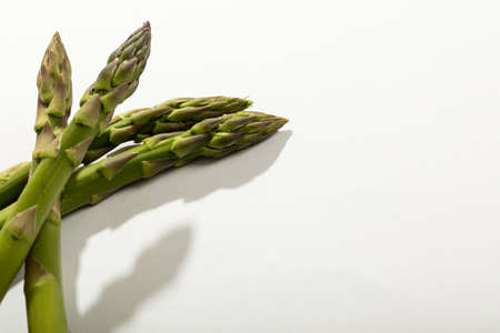 High angle close-up view of raw green asparagus by copy space against white background. unaltered, food, healthy eating and organic concept.の写真素材