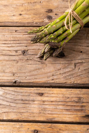Overhead view of string tied raw green asparagus bunches on wooden brown table. unaltered, food, healthy eating and organic concept.の写真素材