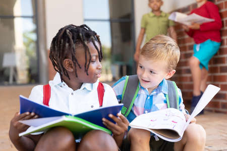 Multiracial elementary schoolboys studying while sitting on floor in school. unaltered, childhood,...