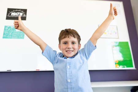 Portrait of smiling caucasian elementary schoolboy with arms raised gesturing thumbs up. unaltered, childhood, education, learning and back to school concept.の写真素材