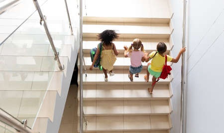 High angle view of multiracial elementary schoolgirls climbing steps in school building. unaltered,...