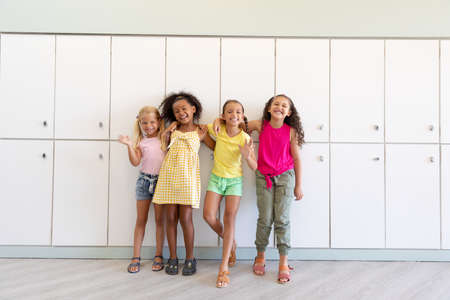Portrait of cheerful multiracial elementary schoolgirls with arm around waiting while standing. unaltered, childhood, together, education, enjoyment and back to school concept.の写真素材