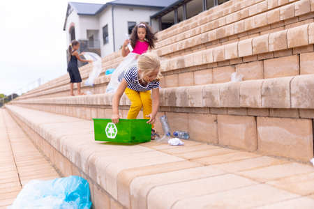 Multiracial elementary schoolgirls cleaning plastic waste on school building steps. unaltered, sustainable lifestyle, education, cleaning, responsibility and recycling concept.の写真素材