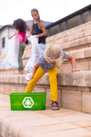 Multiracial elementary schoolgirls collecting plastic waste on school building steps. unaltered, sustainable lifestyle, education, cleaning, responsibility and recycling concept.の写真素材