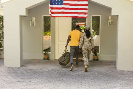 Portrait of happy female mid adult african american soldier entering home with husband. unaltered, pride, homecoming, american flag, military, arrival, armed forces and patriotism.の写真素材