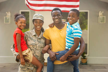 Portrait of happy female mid adult african american soldier with family outside house. unaltered, pride, homecoming, military, arrival, togetherness, armed forces and patriotism concept.の写真素材