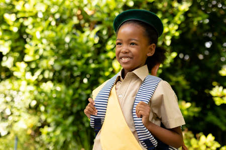 Smiling african american scout girl in uniform with backpack looking away against plants. unaltered, girl scout, childhood, courage, leadership and scouting.の写真素材