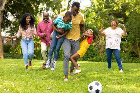 Playful african american multi-generational family playing soccer together in backyard on weekend. unaltered, family, togetherness, weekend and leisure concept.の写真素材