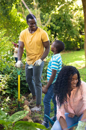 Smiling african american boy gardening with father and mother in backyard on weekend. unaltered,...