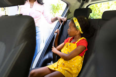 Midsection of african american mother teaching daughter to adjust seat belt while sitting in car....