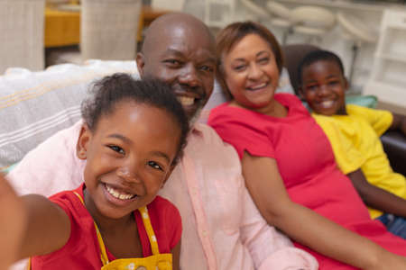 Happy african american girl taking selfie with brother and grandparents at home. unaltered,...