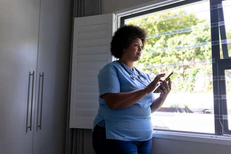 African american mid adult female nurse using digital tablet while standing by window in hospital....