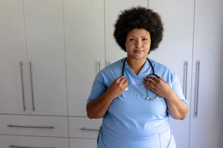 Portrait of confident african american mid adult female nurse with stethoscope standing in hospital. unaltered, healthcare worker, expertise and occupation concept.の写真素材