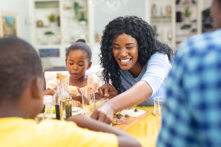Happy african american mid adult woman having lunch with family at home on thanksgiving day. unaltered, family, food, togetherness, cultures and holiday concept.の写真素材