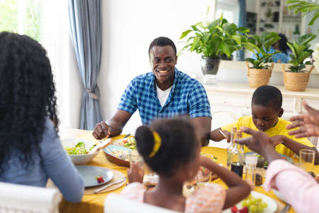 Smiling african american mid adult man having lunch with family at home on thanksgiving day. unaltered, family, food, togetherness, cultures and holiday concept.の写真素材