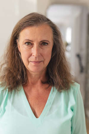 Close-up portrait of confident caucasian senior woman with brown curly hair at home. unaltered,...