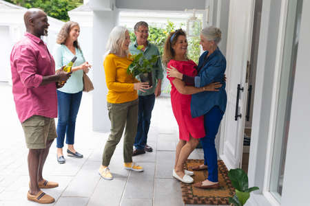 Happy senior woman welcoming multiracial friends at entrance during house party. unaltered, lifestyle, friendship, togetherness, party, leisure and social gathering.の写真素材