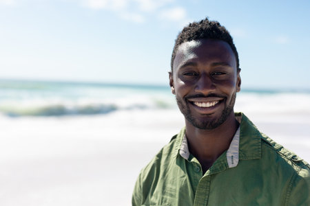 Portrait of happy african american man standing at beach enjoying sunny day. unaltered, lifestyle, enjoyment and summer holiday concept.の写真素材