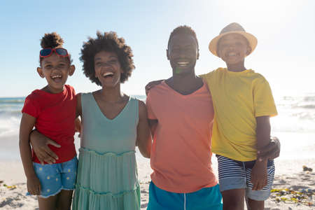 Portrait of smiling african american family with arms around enjoying summer holiday at beach....