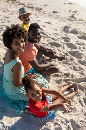 High angle portrait of smiling african american family sitting on sand at beach. unaltered, family, lifestyle, togetherness, enjoyment and holiday concept.の写真素材