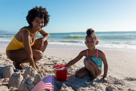 Portrait of smiling african american mother and daughter making sandcastles at beach. unaltered, family, lifestyle, togetherness, enjoyment and holiday concept.の写真素材