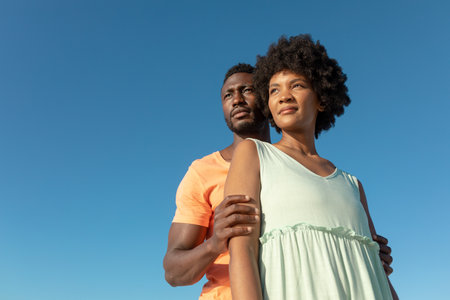 Low angle view of african american couple standing against clear blue sky with copy space....