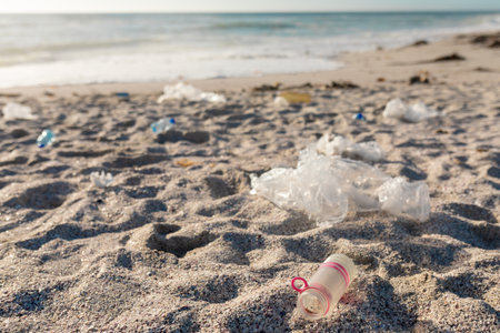 Plastic waste scattered on sand at beach during sunny day. unaltered, environmental damage and plastic pollution concept.の写真素材