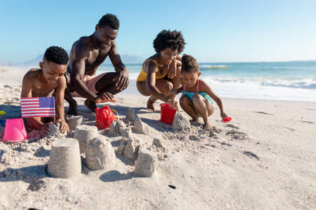 African american family making sandcastles together at beach on sunny day. unaltered, family, lifestyle, togetherness, enjoyment and holiday concept.の写真素材