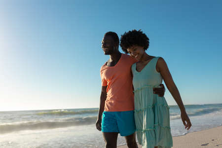 Happy african american couple walking against clear blue sky on sunny day. unaltered, lifestyle, love, togetherness and holiday concept.の写真素材