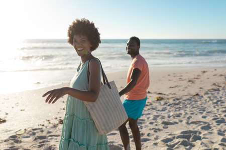Portrait of happy african american woman walking with boyfriend at beach on sunny day. unaltered,...